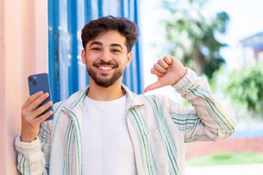 Açık havada cep telefonu kullanan yakışıklı bir Arap gururlu ve kendini beğenmiş.