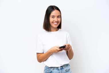 Beyaz arka planda izole edilmiş genç beyaz kadın cep telefonuyla mesaj gönderiyor.