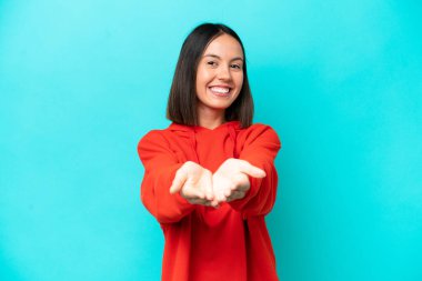 Mavi arka planda izole edilmiş genç beyaz kadın bir ilan vermek için avucunun içinde hayali bir fotokopi makinesi tutuyor.