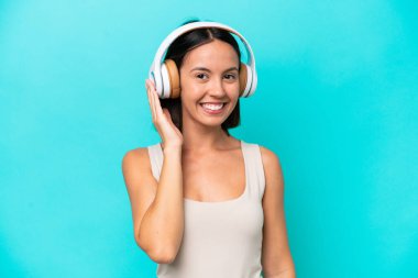 Genç beyaz kadın mavi arka planda izole edilmiş müzik dinliyor.