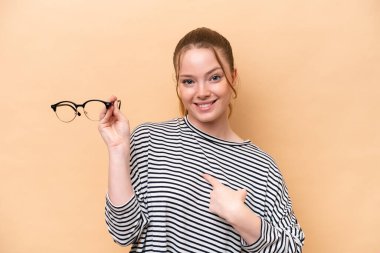 Gözlüklü, bej arka planda, yüzünde sürpriz ifade olan beyaz bir kız.