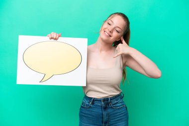 Kafkasyalı genç bir kadın yeşil arka planda izole edilmiş. Elinde konuşma baloncuğu ikonu olan bir levha var ve telefon jesti yapıyor.