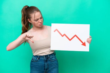Young caucasian woman isolated on green background holding a sign with a decreasing statistics arrow symbol and doing bad signal
