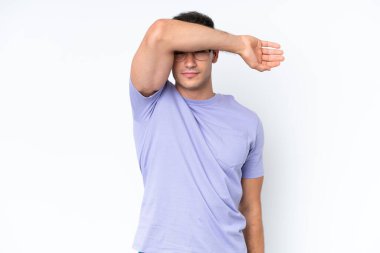 Beyaz arka planda izole edilmiş beyaz tenli genç adam gözlerini elleriyle kapatıyor.