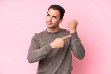 Pembe arka planda izole genç beyaz adam geç kalma jesti yapıyor.