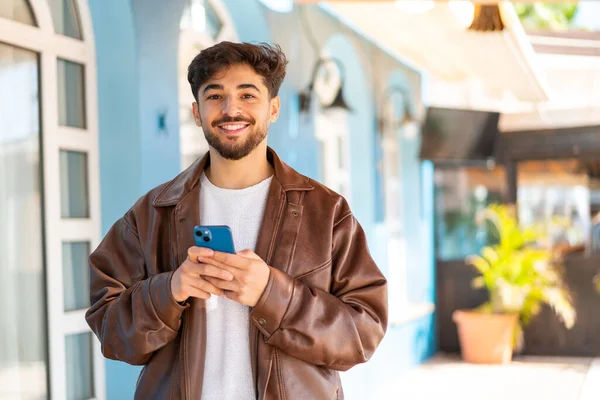 Hezký Arab Muž Venku Dívá Kamery Usmívá Při Používání Mobilu — Stock fotografie