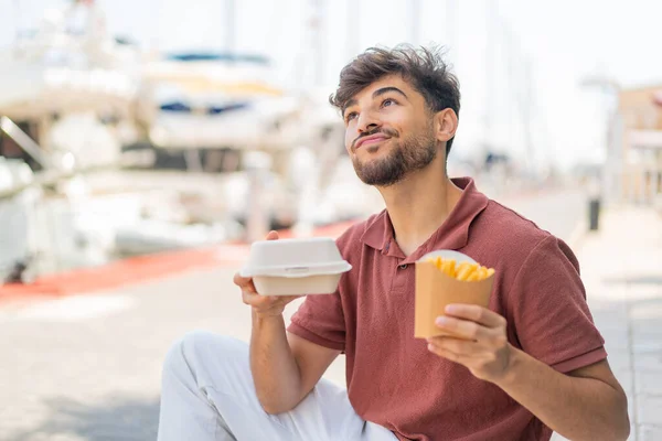 アウトドアの若いアラビアのハンサムな男は 揚げチップを取って 箱の食べ物と考える — ストック写真