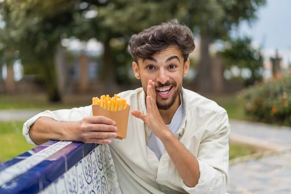 若いアラビアのハンサムな男は 何かを囁く屋外で揚げチップを保持しています — ストック写真