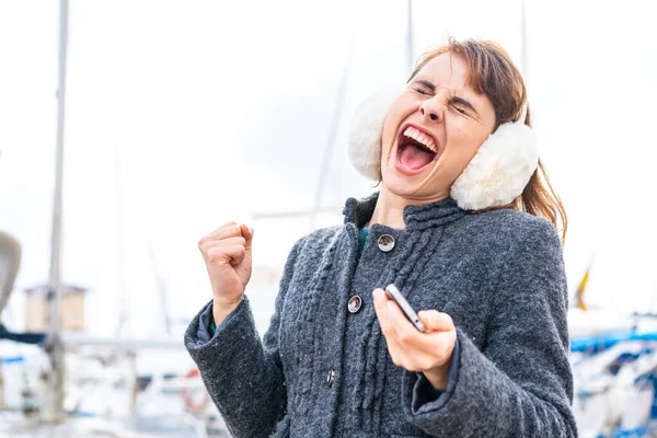 勝利の位置で電話で屋外で冬のマフを着用しているブルネット女性 — ストック写真