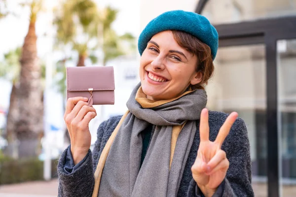 Μπρουνέτ Γυναίκα Κρατώντας Ένα Πορτοφόλι Εξωτερικούς Χώρους Χαμογελώντας Και Δείχνοντας — Φωτογραφία Αρχείου