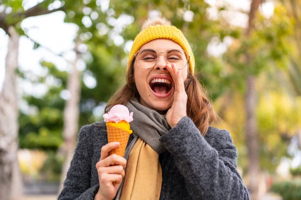 Brunette woman with a cornet ice cream at outdoors shouting with mouth wide open