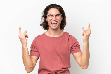 Beyaz arka planda izole edilmiş genç yakışıklı adam boynuz hareketi yapıyor.
