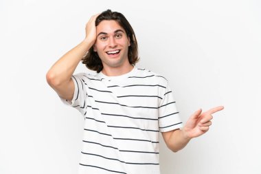 Beyaz arka planda izole edilmiş genç ve yakışıklı bir adam şaşırmış ve işaret ediyor.