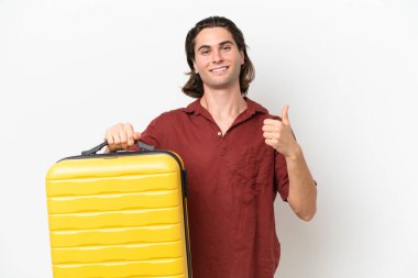 Genç ve yakışıklı bir adam beyaz arka planda izole edilmiş seyahat valiziyle ve başparmağıyla