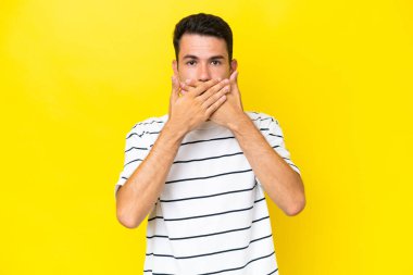 Elleri ile ağız kapsayan izole sarı arka plan üzerinde Genç yakışıklı adam