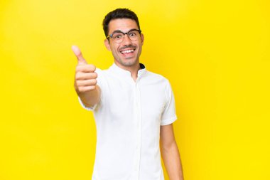 Soyutlanmış sarı arka planda genç ve yakışıklı bir adam. Başparmakları havada. Çünkü iyi bir şey oldu.