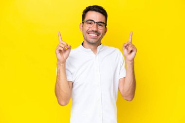 Soyutlanmış sarı arka planı olan yakışıklı genç adam harika bir fikre işaret ediyor.