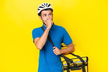 Termal sırt çantalı yakışıklı genç adam izole edilmiş sarı arka planda kuşkuları ve kafa karıştırıcı bir ifadeyle.