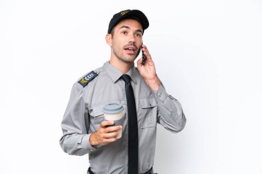 İzole edilmiş beyaz arka planı olan genç güvenlik görevlisi elinde kahve ve bir cep telefonu tutuyor.