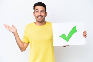 İzole edilmiş beyaz arkaplan üzerinde genç yakışıklı bir adam üzerinde yeşil işaret simgesi olan bir pankart tutuyor.