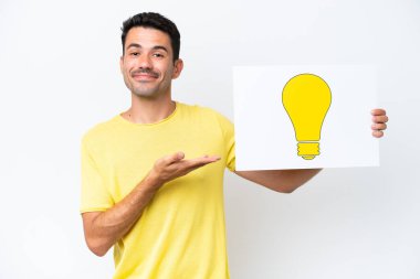 İzole edilmiş beyaz arka planda genç yakışıklı bir adam elinde ampul simgesi olan bir pankart tutuyor ve ona doğrultuyor.