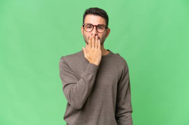 Genç, yakışıklı, beyaz bir adam izole edilmiş arka planda, ağzı eliyle kapatıyor.