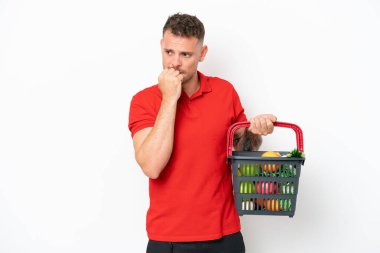 Beyaz arka planda izole edilmiş yiyecek dolu bir alışveriş sepetini tutan beyaz bir genç.