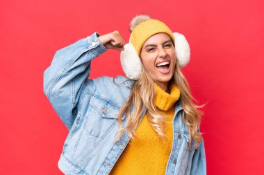 Genç ve güzel Uruguaylı kadın, kırmızı arka planda izole edilmiş kışlık kuklalar takıyor. Güçlü bir hareket yapıyor.