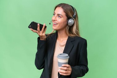 Tele pazarlamacı güzel Uruguaylı kadın izole bir arka planda çalışan kahve ve bir cep telefonuyla.