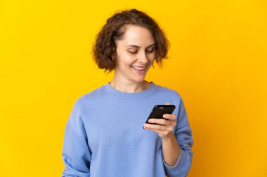 Pembe arka planda izole edilmiş genç bir İngiliz kadın cep telefonuyla mesaj ya da e-posta gönderiyor.