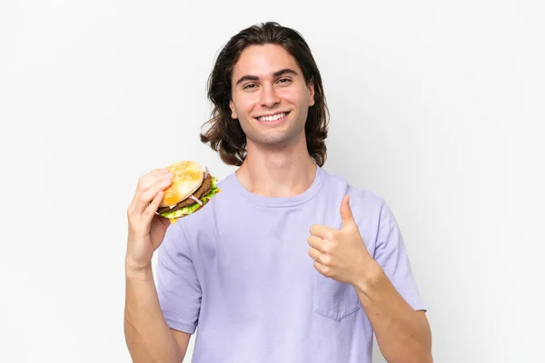 良いことが起こったので 親指で白い背景に隔離されたハンバーガーを保持している若いハンサムな男 — ストック写真