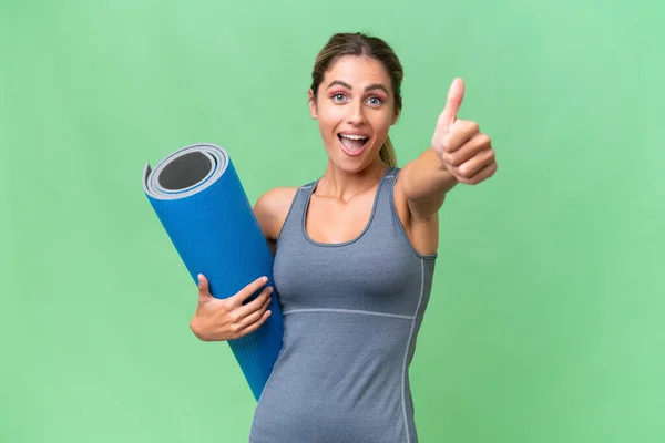 stock image Pretty Young Uruguayan sport woman going to yoga classes while holding a mat over isolated background with thumbs up because something good has happened