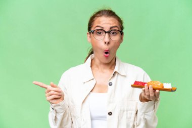 Kafkasyalı genç bir kadın soyutlanmış arka planda saşimi tutuyor şaşırmış ve işaret ediyor.