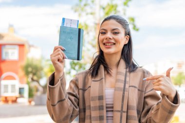 Dışarıda elinde pasaport tutan genç ve güzel bir kadın. Sürpriz bir yüz ifadesi.