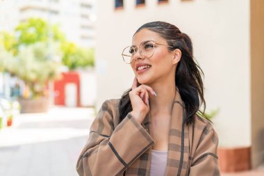 Dışarıda gözlüklü genç bir kadın yukarı bakarken bir fikir düşünüyor.