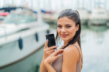 Dışarıda cep telefonu kullanan genç ve güzel bir kadın çok fazla gülümsüyor.