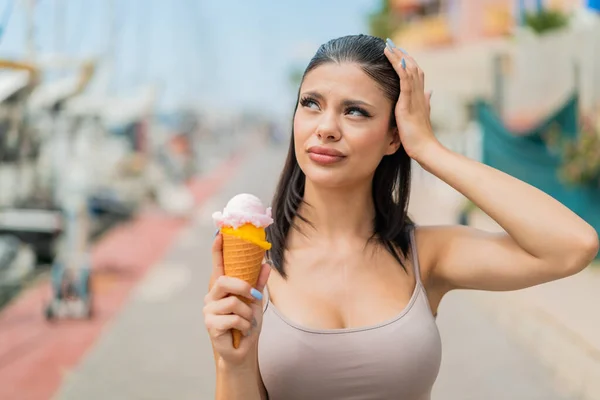 Young pretty woman with a cornet ice cream at outdoors having doubts and with confuse face expression