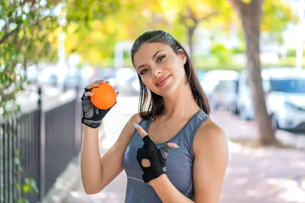 年轻漂亮的女运动员在户外拿着橙子指着它 — 图库照片