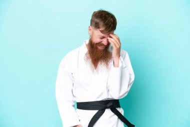 Uzun sakallı kızıl saçlı adam mavi arka planda karate yapıyor.