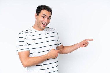 Beyaz arka planda izole edilmiş genç beyaz adam şaşırmış ve işaret ediyor.