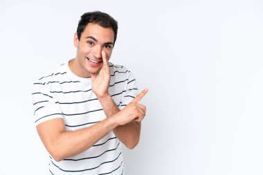 Beyaz arka planda izole edilmiş genç beyaz bir adam bir ürün sunmak ve bir şeyler fısıldamak için kenarı işaret ediyor.