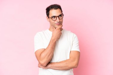 Kafkasyalı genç bir adam pembe arka planda izole edilmiş, yukarı bakarken bir fikir düşünüyor.