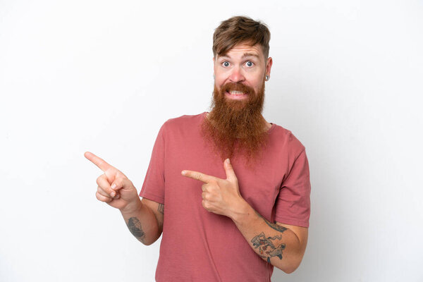 Redhead man with long beard isolated on white background frightened and pointing to the side
