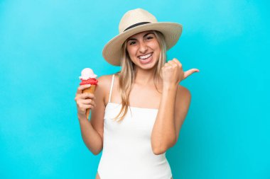 Mavi arka planda izole edilmiş kornet dondurması olan mayo giymiş beyaz bir kadın bir ürünü sunmak için yan tarafı işaret ediyor.