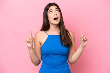 Pembe arka planda izole edilmiş genç Brezilyalı kadın şaşırmış ve işaret ediyor.