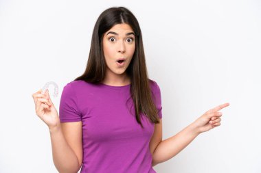 Beyaz arka planda izole edilmiş görünmez diş telleri tutan genç Brezilyalı kadın şaşırmış ve işaret ediyor.
