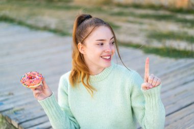 Dışarıda donut tutan genç ve güzel bir kız. Çözümün ne olduğunu anlamak için parmağını kaldırıyor.