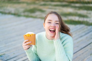 Dışarıda patates kızartması tutan güzel bir kız ağzı açık bağırıyor.