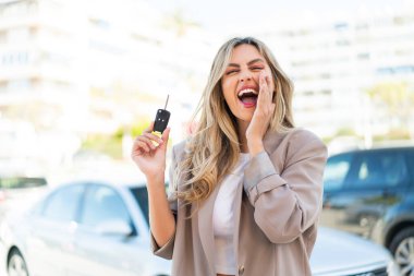 Güzel sarışın Uruguaylı kadın arabanın anahtarlarını tutuyor ve ağzı açık bağırıyor.