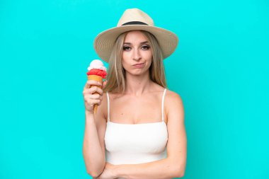 Mayo giymiş sarışın bir kadın elinde dondurma tutuyor. Mavi arka planda, üzgün bir ifadeyle izole edilmiş.
